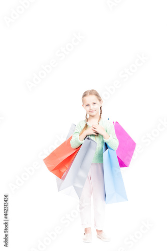 Studio portrait shot of beautiful little girl with two braids wearing casual clothes holding shopping bags looking at camera, white background