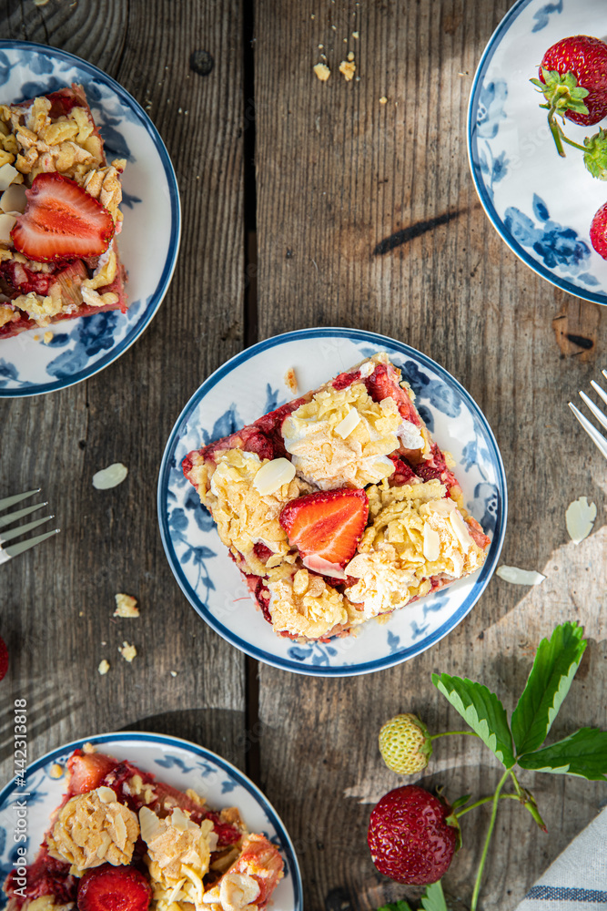 Strawberry and rhubarb meringue crumble squares on white and blue plates on wooden table. Strawberry and rhubarb meringue crumble squares on white and blue plates on wooden table.