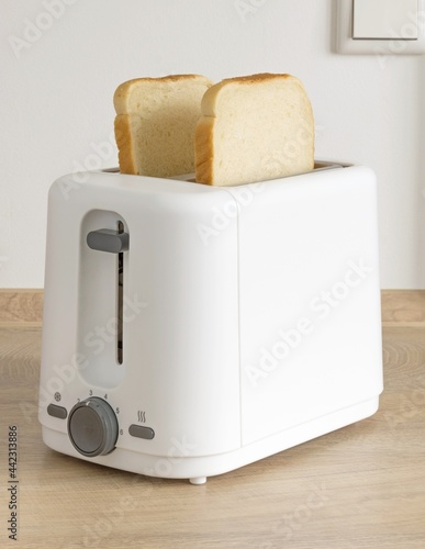 Two slices of white bread ready for toasting in an electrical toaster on a wooden kitchen worktop table