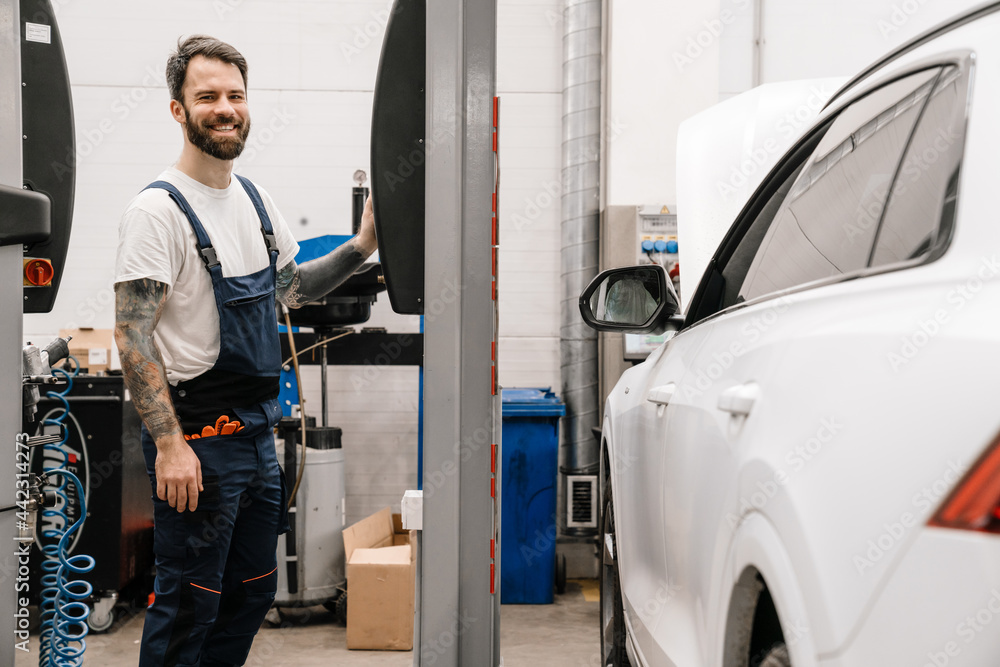 Bearded smiling car mechanic testing car while working in garage