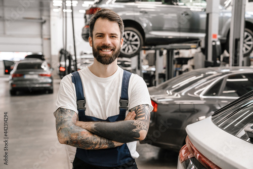 Bearded white car mechanic smiling while standing in garage indoors © Drobot Dean