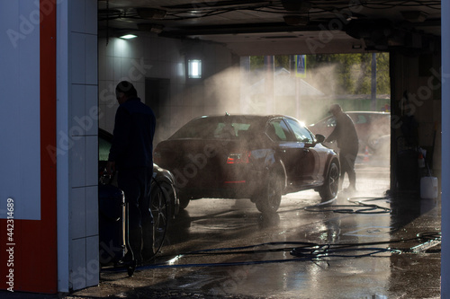 Car wash at a car wash. Workers wash their cars under the pressure of water.