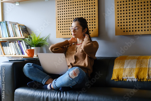 Young casual smart woman suffering neck pain and stuying at home using her laptop. photo