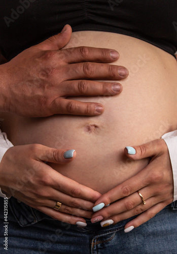 Parents' hands lie on the pregnant belly of a woman. Sensual photo of young parents waiting for their baby
