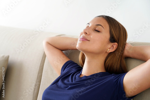 Close up of calm beautiful woman resting sleeping with hands behind head on couch at home. Peaceful young female leaning back with closed eyes, napping on cozy sofa.