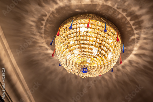 Wonderful round glowing luster with shiny glass beads on white ceiling with shadows patterns in theater hall low angle shot