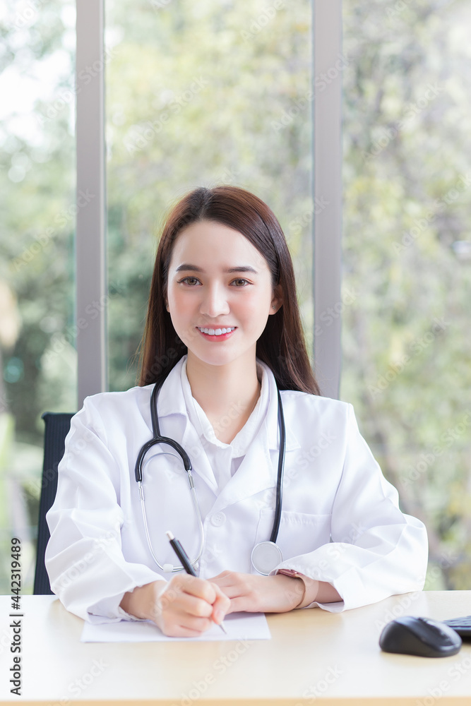 Asian professional woman doctor is writing something on the paper while sits and works in office room at hospital in health care and coronavirus protection concept.