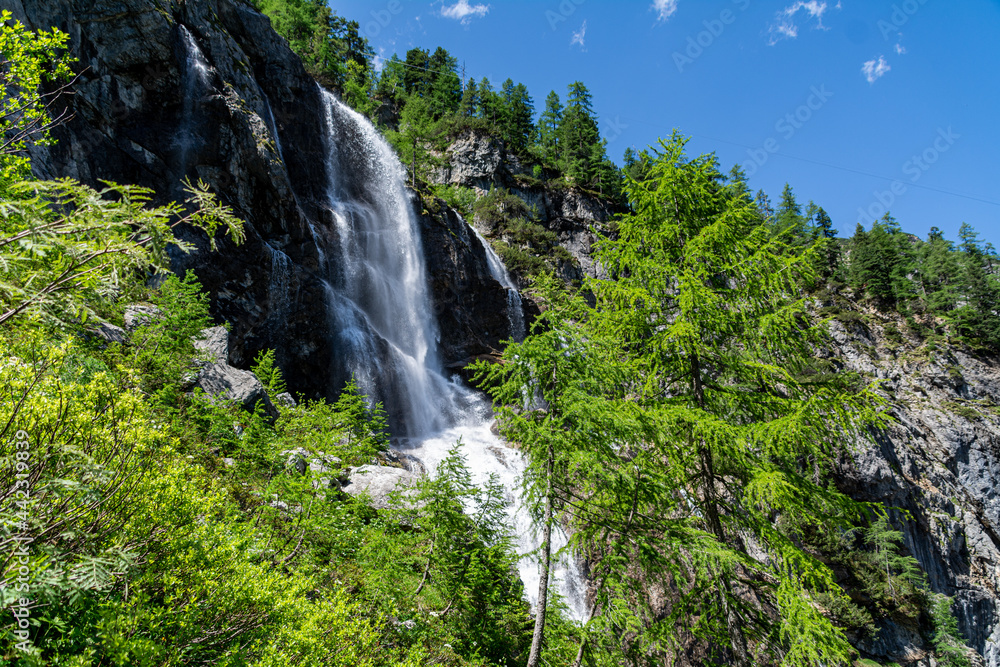 A waterfall in the Austrian Alps on a sunny summer day with rocks and trees