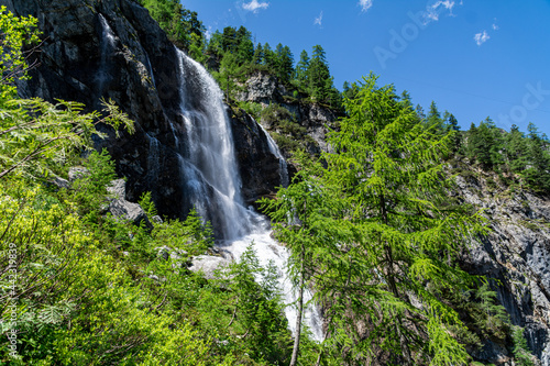 A waterfall in the Austrian Alps on a sunny summer day with rocks and trees