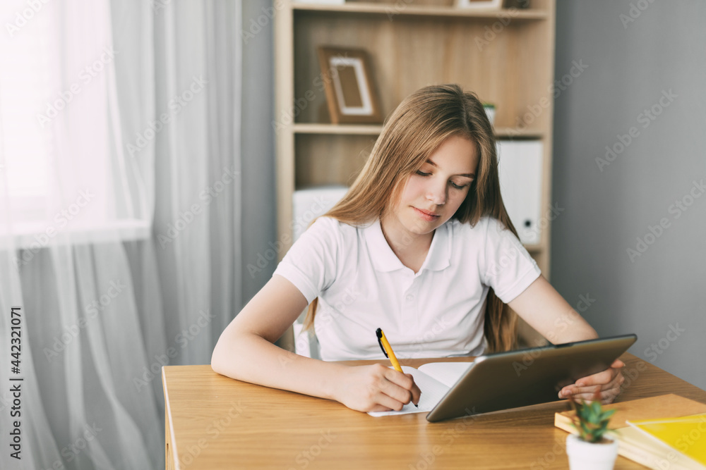 An attractive student is studying an online course and taking notes while preparing for the exam with a tablet. The concept of education and upbringing, preparation for exams An attractive student is studying an online course and taking notes while preparing for the exam with a tablet. The concept of education and upbringing, preparation for exams