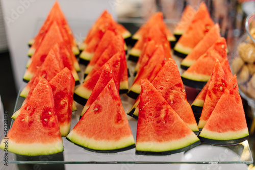 Slices of sliced watermelon are lying on glass table of fruit buffet. Healthy food. Natural desserts. Lifestyle. Freshness and coolness.