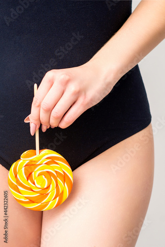 Woman holding lollipop candy on bikini zone, the concept of intimate depilation, problems of intimate hygiene