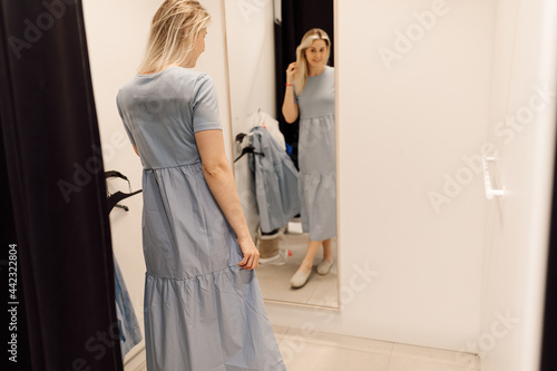 Beautiful blonde is in great mood during fitting of dress that suits her very well. Organization of sales process in supermarkets. Fashionable clothes. Shopping and pleasure. Convenience and comfort.