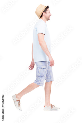 Vertical full length side view portrait of handsome bearded Caucasian man wearing summer outfit with hat walking somewhere, white background
