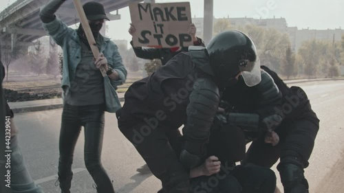 Slowmo tracking shot of two riot police officers in full gear running up to male protester and arresting him
