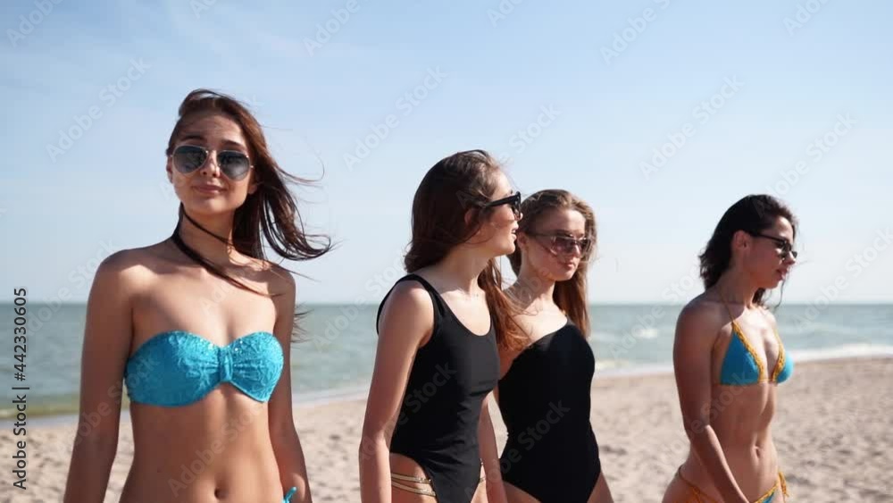 Group of pretty female friends having fun walking down sandy tropical beach in swimsuits. Interracial women chatting and laughing on summer day outdoors. Girls wearing bikini and swimwear by the sea. Group of pretty female friends having fun walking down sandy tropical beach in swimsuits. Interracial women chatting and laughing on summer day outdoors. Girls wearing bikini and swimwear by the sea.