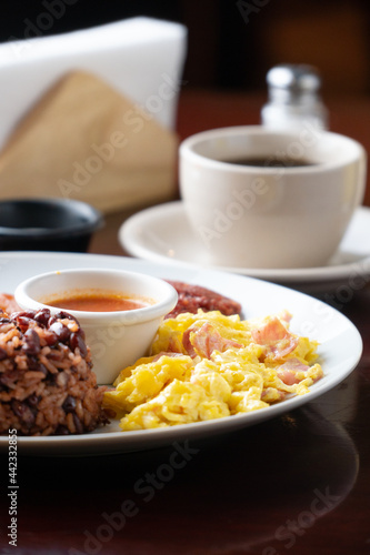 Latin breakfast with fried plantain, scrambled eggs, ground beans, chorizo ​​and orange juice or coffee, all on a white plate