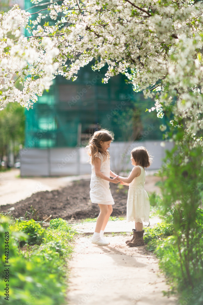 Cute little girls kids girlfriends hugging among the foliage and flowers, the concept of girlish friendship and secrets, childhood in summer Cute little girls kids girlfriends hugging among the foliage and flowers, the concept of girlish friendship and secrets, childhood in summer