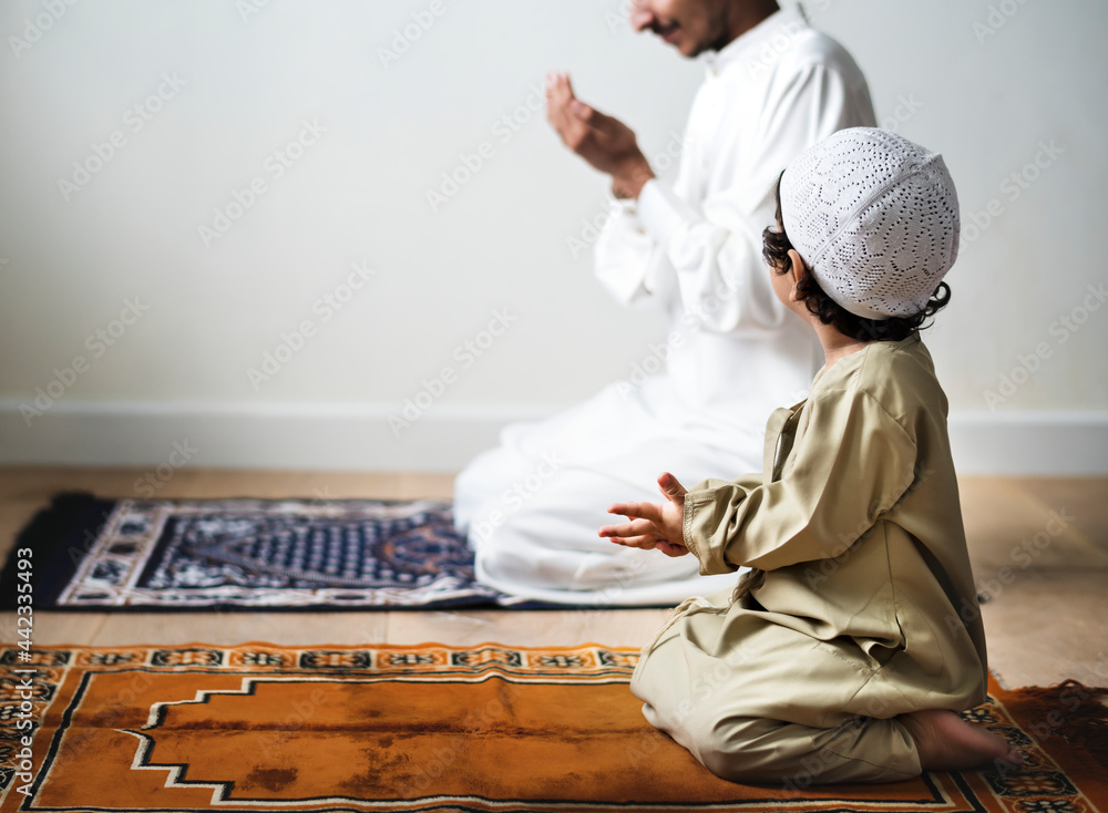Fototapeta premium Little boy praying alongside his father during Ramadan