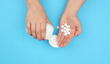 female hand holding round white pills on a blue background, pain treatment