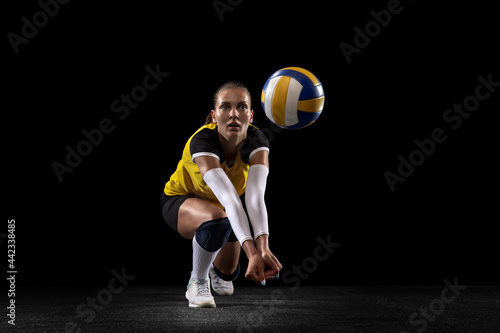 Female professional volleyball player with ball isolated on black studio background. The athlete, exercise, action, sport, healthy lifestyle, training, fitness concept. photo