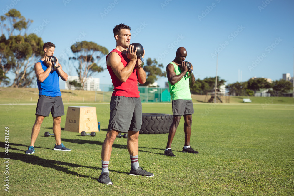 Diverse group of muscular men exercising with kettle bells outdoors Diverse group of muscular men exercising with kettle bells outdoors