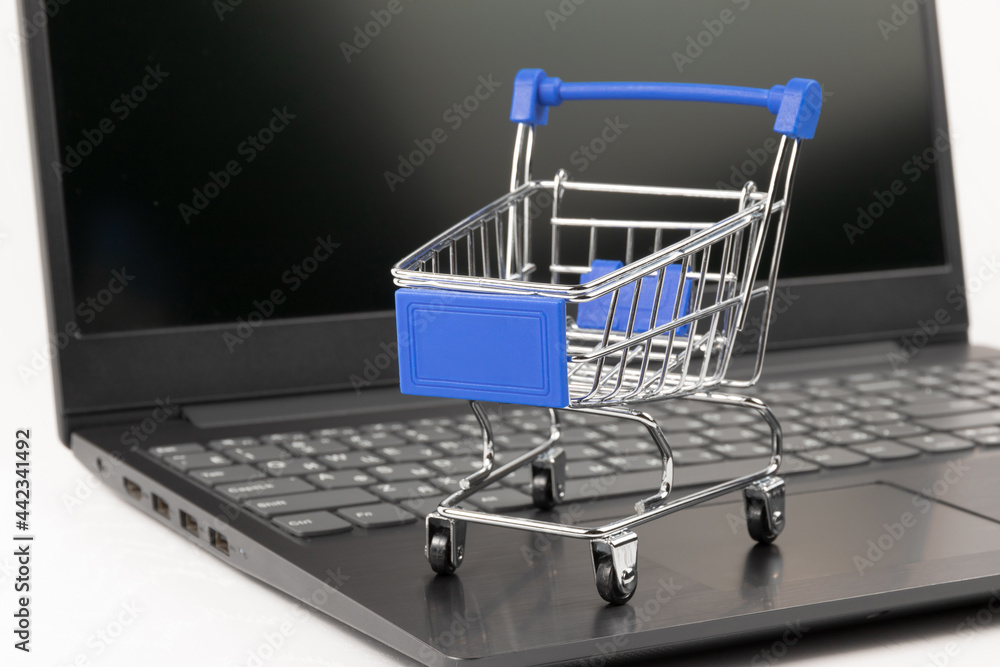 metal chrome grocery cart on wheels against the background of a black laptop on a white wooden table. selective focus