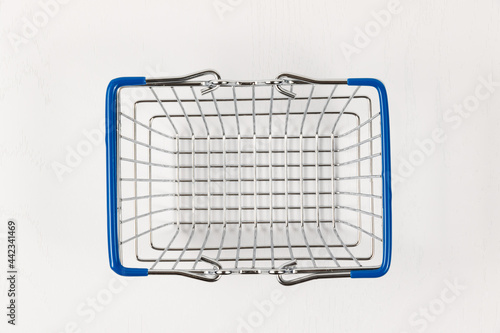 empty metal shiny basket with grocery handles on white wooden table background. close-up photo