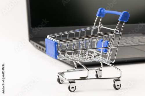 metal chrome grocery cart on wheels against the background of a black laptop on a white wooden table. selective focus