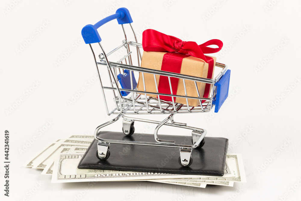 metal chrome shiny shopping trolley on wheels with gift box on wallet with dollars on white background. selective focus