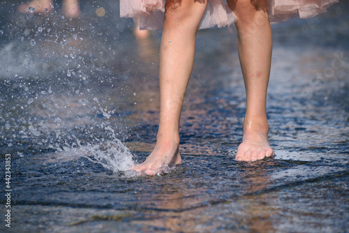 Little girl bare feet playing with a fountain water jet at the square of the city © Yurii Zushchyk