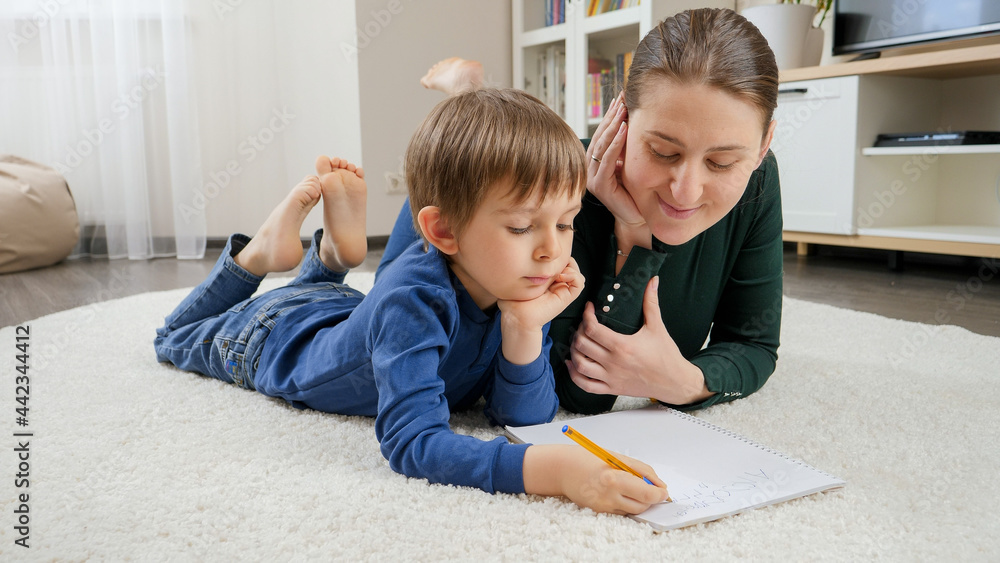 Young mother teaching and helping her son doing homework on floor at home. Concept of domestic education, child development and happy parenting Young mother teaching and helping her son doing homework on floor at home. Concept of domestic education, child development and happy parenting