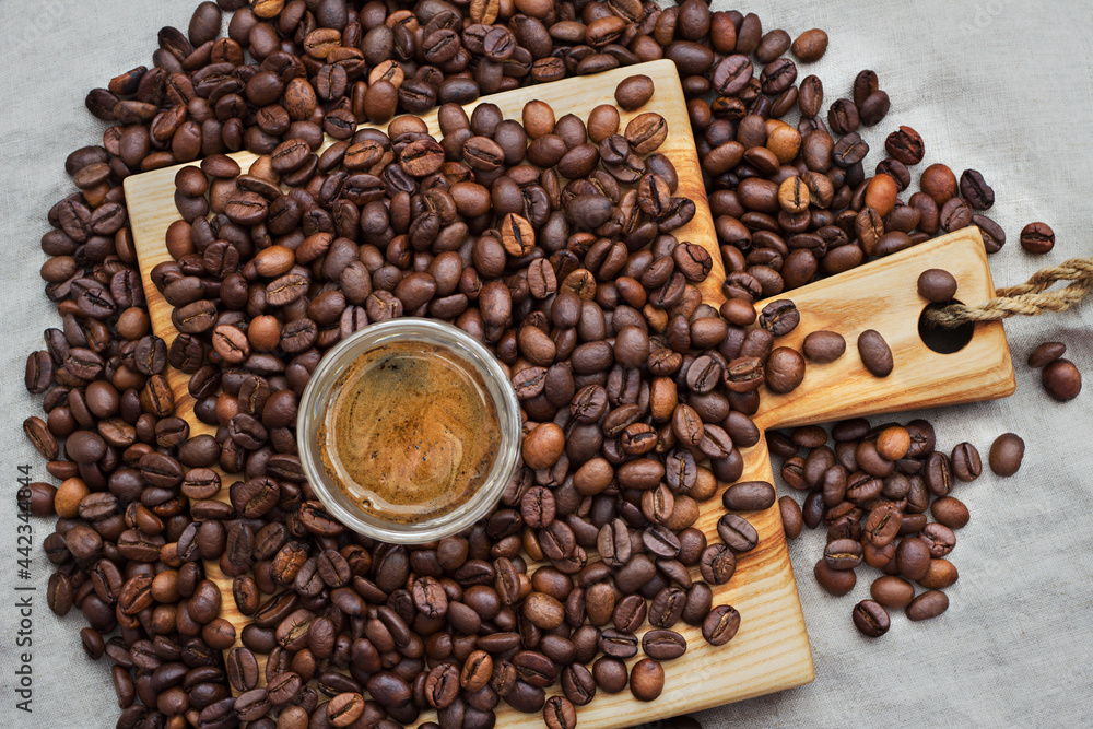 Naklejka premium Small glass shot of coffee among selected and calibrated Arabica coffee beans scattered on a napkin, table, blended, top view