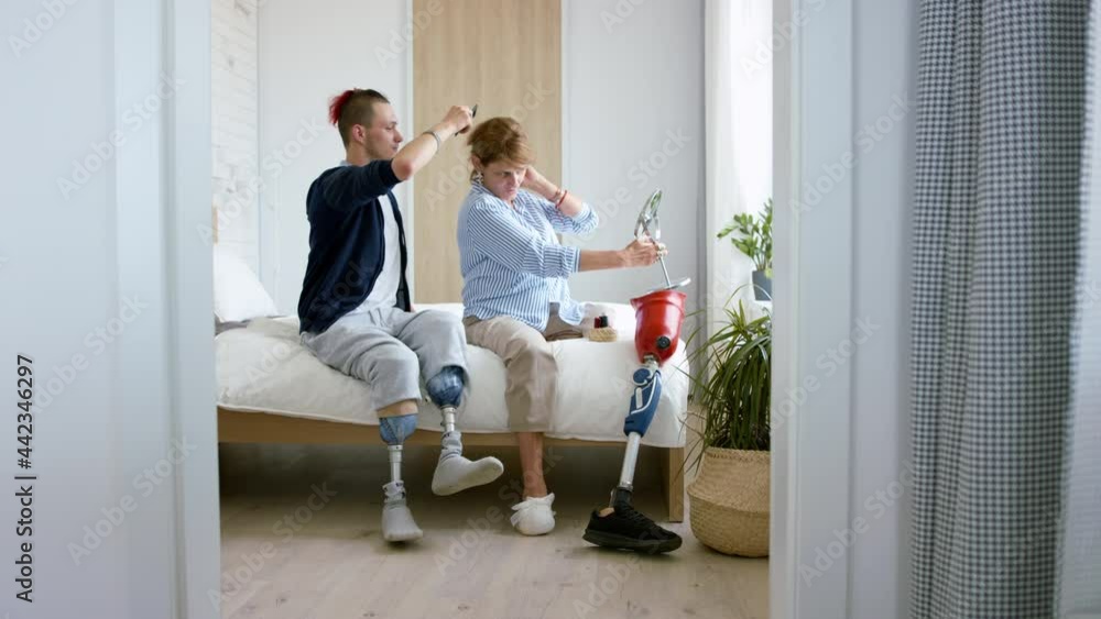 Disabled son helping his disabled mom with hair on bed. Morning routine with leg amputee concept. Disabled son helping his disabled mom with hair on bed. Morning routine with leg amputee concept.