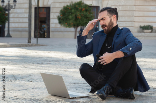 Schilderij op canvas Caucasian young businessman lamenting looking at his laptop sitting on the stree