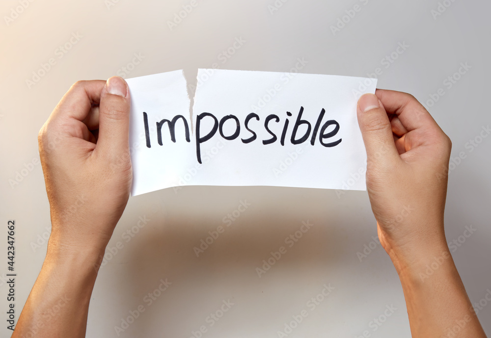 Hands tearing a white paper with the text impossible Hands tearing a white paper with the text impossible
