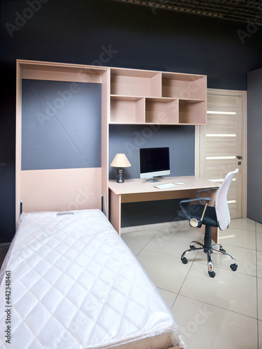 Bedroom interior with yellow unfolded Vertical Mount Murphy Wall Bed, pull out bed stored into working place with table armchair shelves and computer, minimalist interior design, modern architecture. photo