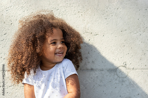 Outdoor portrait of a smiling girl. Curly african american girl is standing by a concrete wall.
