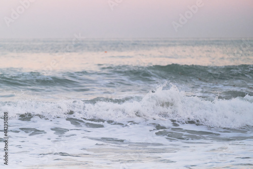 Minimalist seascape. Blue clear sea water and white foam from waves against background of horizon and bright delicate pink dawn sky in the morning.