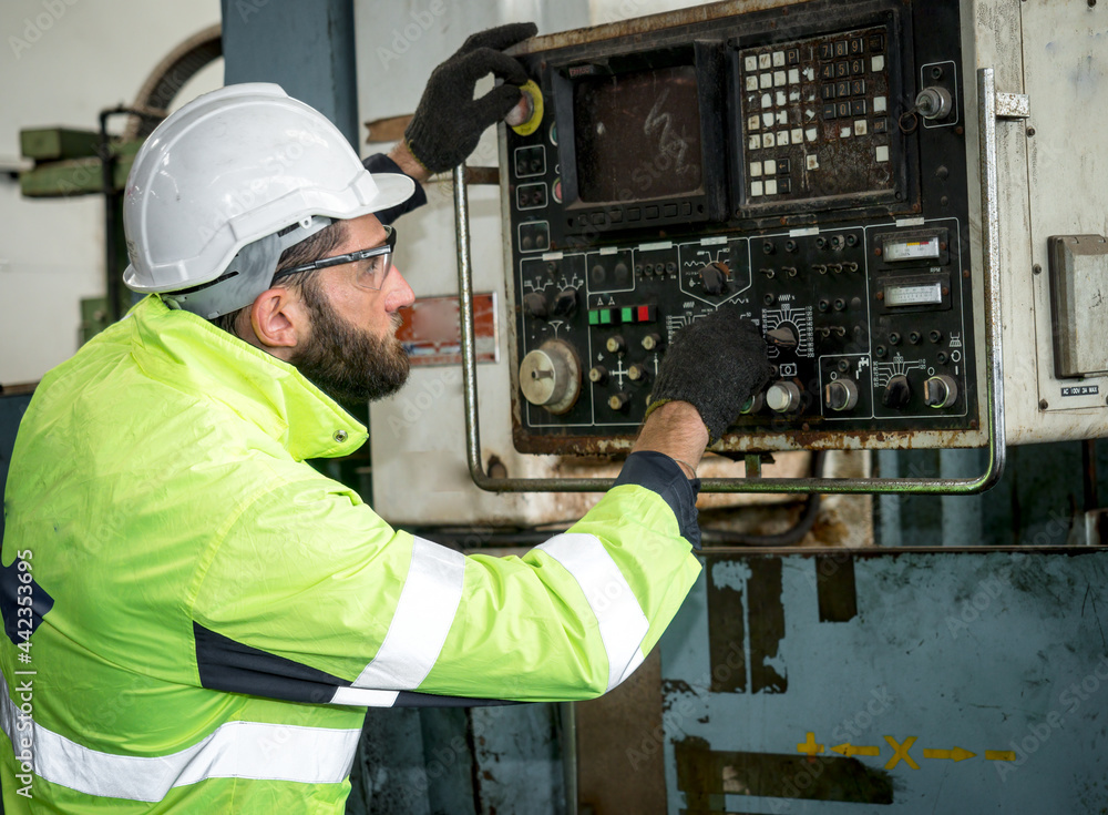A Confidence handsome man mechanical worker in a protective uniform, helmet controls the CNC Machinery while working at the plant. A Confidence handsome man mechanical worker in a protective uniform, helmet controls the CNC Machinery while working at the plant.