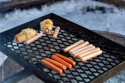 Sausages and sausage buns on a barbecue grill over a fire.