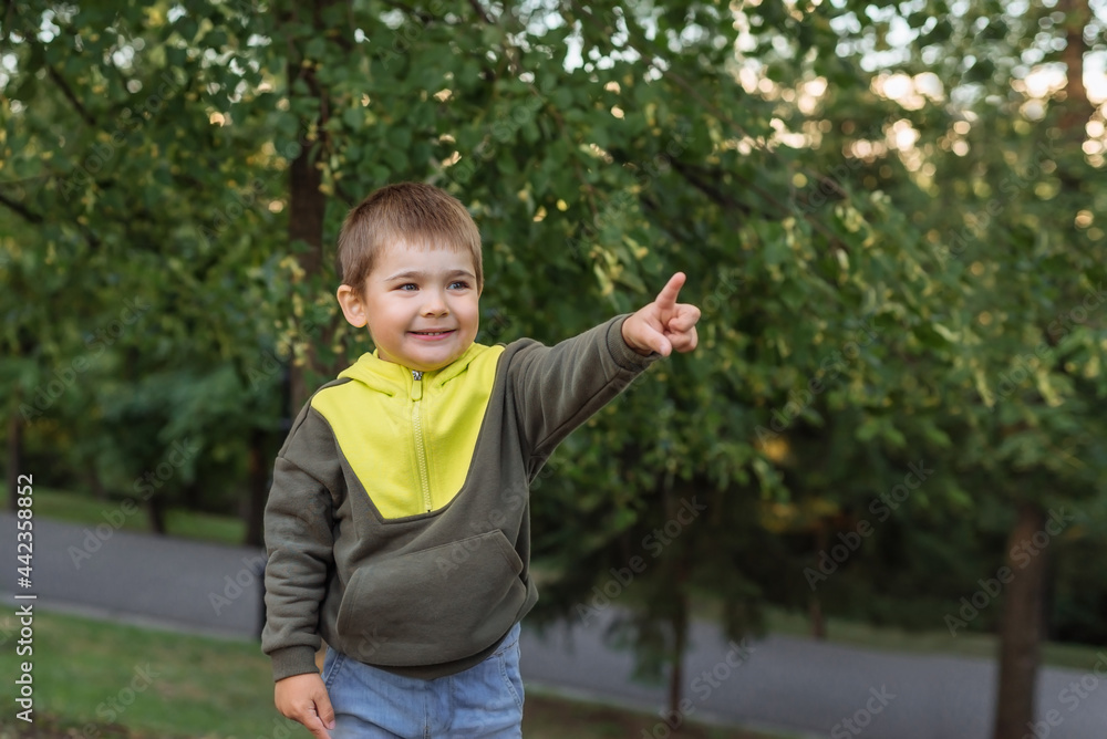 a happy little Caucasian child points his finger in the park. portrait of a cheerful child a happy little Caucasian child points his finger in the park. portrait of a cheerful child
