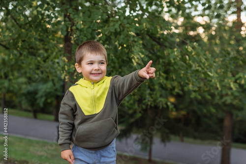 a happy little Caucasian child points his finger in the park. portrait of a cheerful child