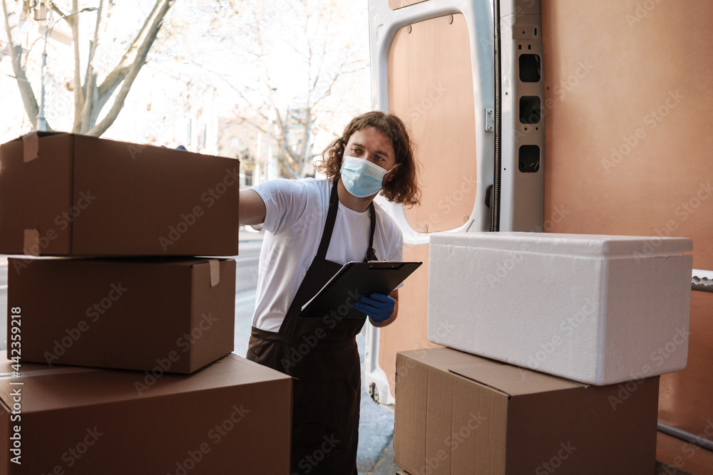 Young white cafe worker in face mask writing while taking delivery Young white cafe worker in face mask writing while taking delivery