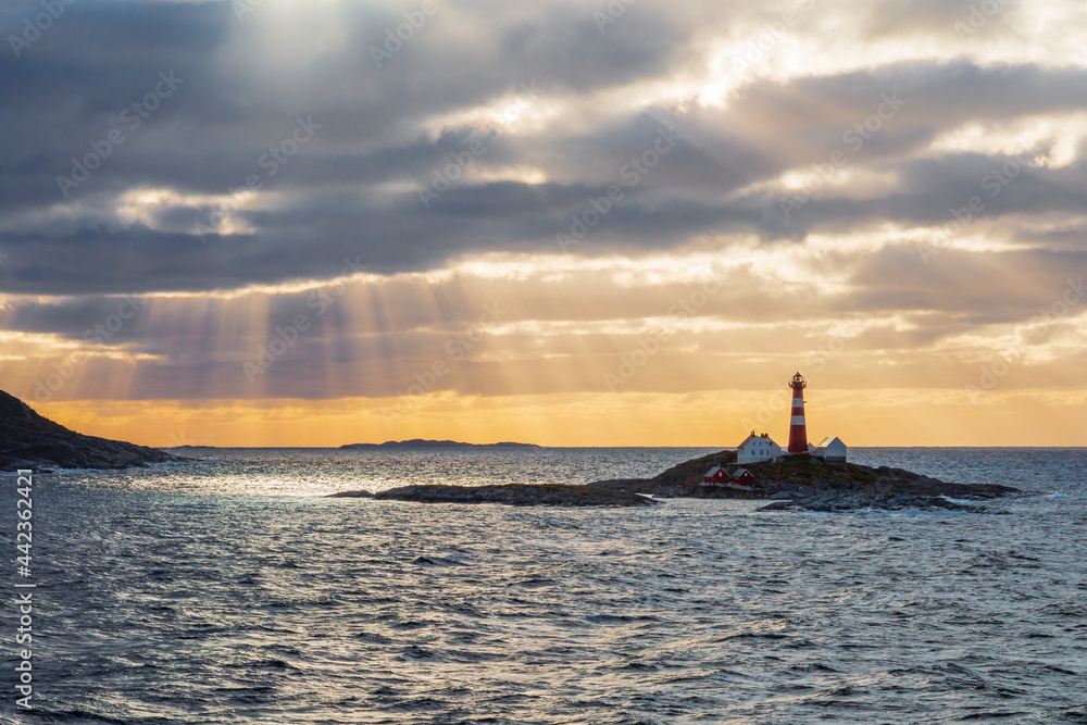 Lighthouse on a small island along the Norwegian coast. The atmosphere was beautiful with the sun rays piercing through the clouds creating a silhouette and beautiful colors.