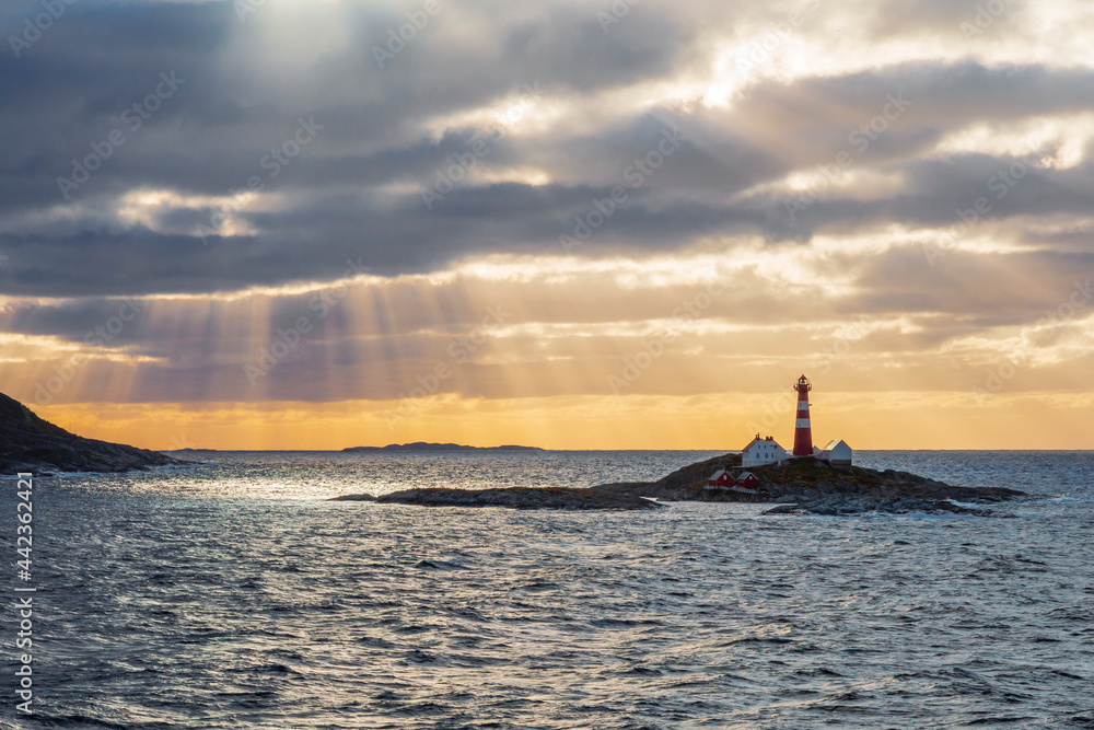 Lighthouse on a small island along the Norwegian coast. The atmosphere was beautiful with the sun rays piercing through the clouds creating a silhouette and beautiful colors. Lighthouse on a small island along the Norwegian coast. The atmosphere was beautiful with the sun rays piercing through the clouds creating a silhouette and beautiful colors.