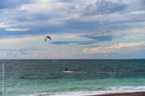View of the sea coast on a summer evening. Sea to horizon from white to dark turquoise. Cloudy sky with evening colors. Silhouettes of a kitesurfer with a parachute. Extreme tourism in summer 