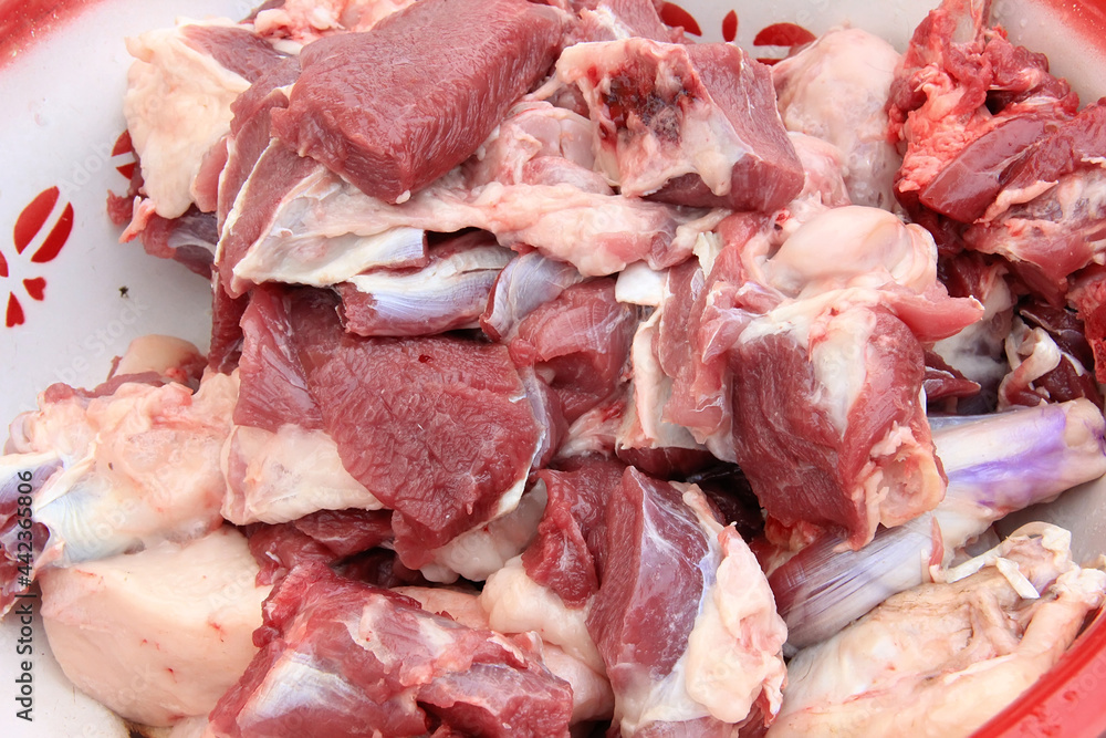 Raw lamb meat cut into large pieces and lamb fat in a cup, close-up
