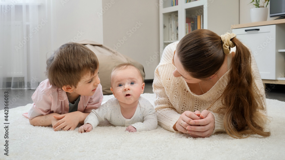 Happy smiling family lying on big carpet at living room and smiling in camera. Parenting, children happiness and family relationship