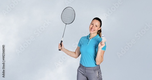 Portrait of caucasian female badminton player holding racket smiling against grey background